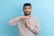 © khosrork - Timeout. Portrait of young handsome businessman standing with serious face and looking at camera with timeout gesture, wearing striped shirt. Indoor studio shot isolated on blue background.