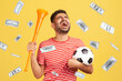 © khosrork - Money rain and rich lucky man extremely happy, holding soccer ball, celebrating victory of favourite football soccer team and his betting. Indoor studio shot isolated on yellow background