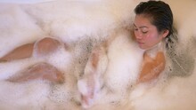 TOP DOWN, CLOSE UP: Beautiful Woman Washing Herself While Having A Bubble Bath. Beautiful Philippine Lady Cleansing Her Arms And Neck In Bathtub. Relaxation Time And Spa Treatment At The End Of Day.