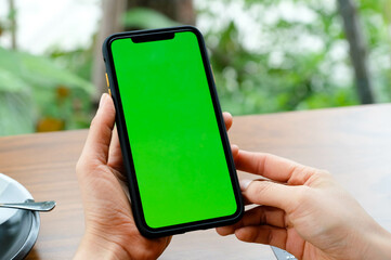 mockup image of a business people holding smart mobile phone with blank green screen on vintage wood