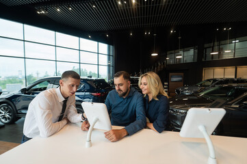 Caucasian married couple chooses a car in a car dealership on digital tablets. 