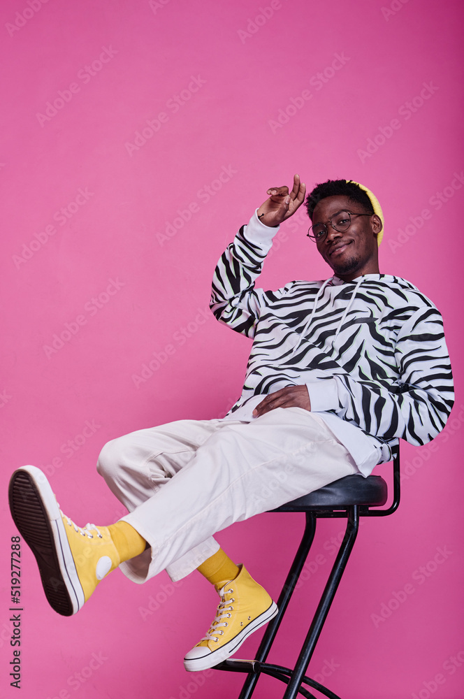 Portrait of African teenage boy in stylish clothes sitting on chair and ...