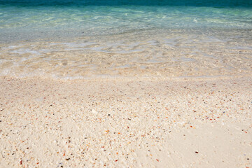 Emerald ocean with foam wave sea on bright beach and gravel texture background for summer vacation season