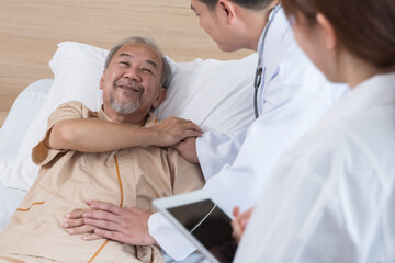 Asian doctor and nurse visit and take care senior man patient in room. Attractive two therapist practitioner explain diagnosis in hospital ward to treatment to elderly older male during appointment.