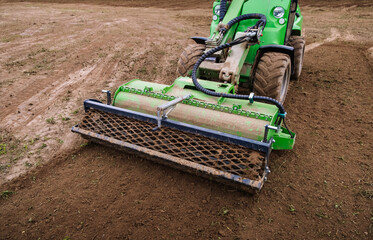 Wall Mural - Mini skid steer loader clear the construction site. Land work by the territory improvement. Small tractor with a rotary cultivator attachment and ground leveler for moving soil. Agriculture machine