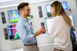 © NDABCREATIVITY - Happy seller man helping to woman to buy a new digital smart device in tech store.