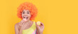 happy kid in swimsuit wearing orange curly wig hair eating french macaron. Teenager child with sweets, poster banner header, copy space.