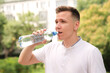 © Евгений Шемякин - Portrait of handsome guy, young happy thirsty man runner is drinking pure fresh water from plastic bottle at warm sunny summer day outdoors after running, jogging, training outside. Healthy habit
