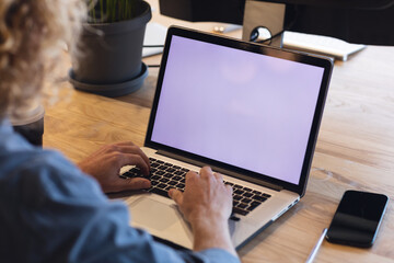 Young caucasian businessman using laptop at desk in creative office, copy space