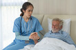 © winnievinzence - Asian female caregiver holding senior man hand giving support and empathy. woman taking care of patient on bed in nursing home. healthcare and medical insurance concept