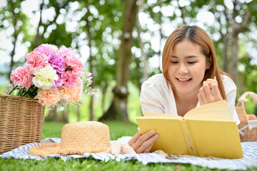 Attractive young Asian female picnicking in the green park, relaxes while reading a book.