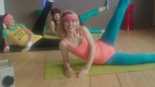 Young And Healthy Caucasian Women And Man In Retro Outfits Lying On Workout Mats In Studio At Daytime, Doing Air Cycling Exercise To Tape Recorder, Looking And Smiling On Camera