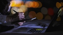 Woman Taking Notes, Paying Bills Online By Credit Card And Analyzing Her Credit Card Statement While Sitting At Bed By The Window At Night. Light Night City, Light Bokeh On Background.  