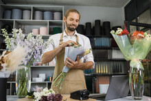 Portrait Of Male Florist In Apron Working In Flower Shop Composing Bouquets With Fresh Flowers For Sale, Floris Making Workshop For Young Employee During Time In Greenery.