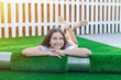 Smiling young caucasian girl lying on her terrace on a new roll of artificial turf. Nice artificial grass ready to lay