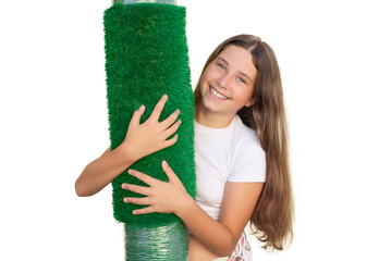 Wall Mural - Young smiling Caucasian girl holding a roll of artificial grass on white background. Soft touch of an artificial turf sheet.