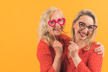 Middle-aged cheerful lovely women in red shirts with white dots smiling at camera, holding fake colorful glasses. High quality photo