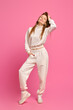 Active woman in white fleece sweatshirt and sweatpants posing over bright pink background