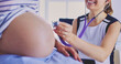 © lenets_tan - Young woman doctor with stethoscope and tablet speaking with pregnant woman at hospital.