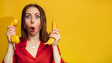 Funny face with a banana and a phone handset. A young woman with a smile holds a banana in her hand. Funny expressions. The concept of nutrition. Yellow style. Vitamins. Empty space for your text or