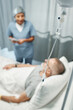 Selective focus on foreground shot of mature man getting IV therapy in modern hospital talking to his doctor