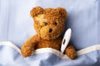 Sick teddy bear on hospital bed with thermometer and plaster patch on head. Pediatrical and child medicine concept