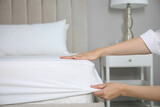 Fototapeta  - Woman putting white fitted sheet over mattress on bed indoors, closeup