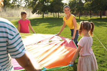 Wall Mural - Group of children and teacher playing with rainbow playground parachute on green grass. Summer camp activity