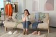 Thoughtful young woman on sofa with clothes at home