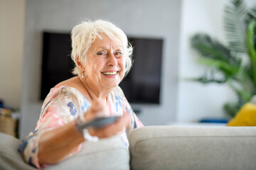 Wall Mural - Active beautiful senior woman in the living room with remote control