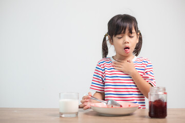 Asian children girls eating bread and desserts and sticking in one's throats with choked food or puke  on the table at home for breakfast or lunch