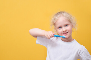 little toddler girl 6 years old holding toothbrush in hand, brushing tooth, yellow background