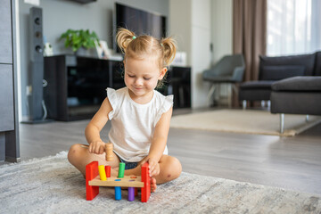 Cute caucasian little girl playing on the floor at home with eco wooden toys. Montessori toy. The child playing educational games.