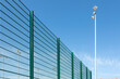 Modern fencing of the sports ground with a metal green fence. Lighting devices in the background