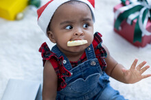 African American Baby Girl Wearing Santa Hat Sitting On Fur In Room, Enjoy Cookie In Mount,  Christmas Time, Holiday Season, Looking At Camera