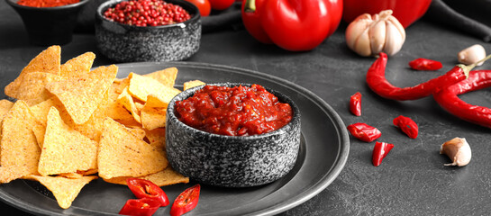 Bowl of tasty sauce and nachos on dark background