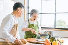 家で一緒に料理を作る笑顔の日本人老夫婦（高齢者）
