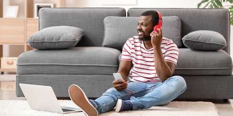 Poster - Handsome African-American man with phone and laptop listening to music at home