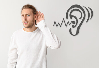 Young man with hearing problem on light background