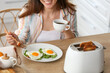 © Pixel-Shot - Beautiful young Asian woman drinking coffee and eating tasty toasts with fried eggs in kitchen
