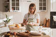 © Natalya - charming young woman in chef's apron preparing pie at home in the kitchen Cozy home interior