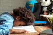 Sad bored African-American girl doing homework at home at her desk,buried in a textbook.Back to school concept.School distance education,home schooling,diverse people.Selective focus.