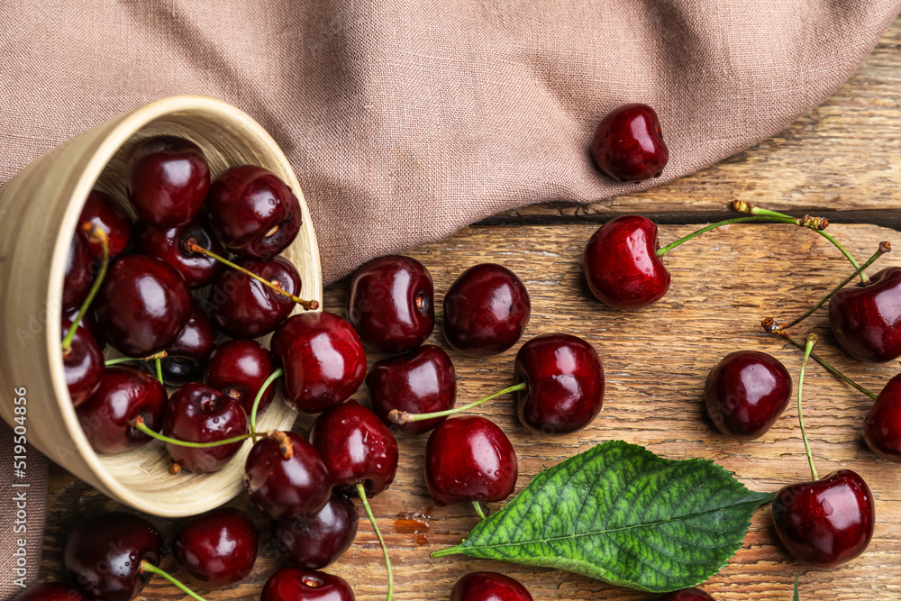 Overturned bowl with tasty cherry on wooden table
