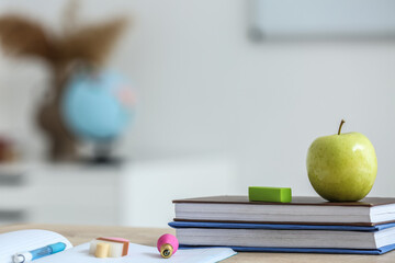 Wall Mural - Apple with school books and erasers on table in classroom