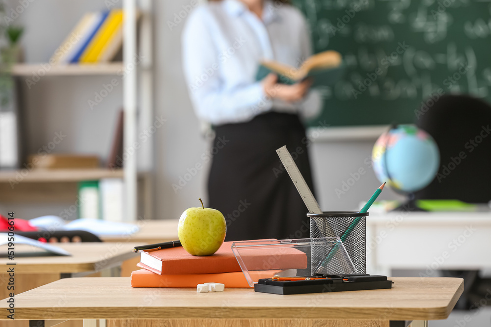 Apple with books, pen cup and school stationery on table in classroom