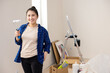 A young woman of Asian origin holds a paint roller in her right hand and is very happy that the long-dreamed-of renovation in her apartment has begun.