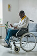 African mature man with disability concentrating on his online work on laptop sitting in wheelchair in living room