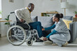 © AnnaStills - African young girl helping senior man with disability to sit on wheelchair, she caring about him at home