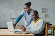 © AnnaStills - Young caregiver pointing at laptop and explaining man with disability how to pay online with credit card