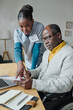 © AnnaStills - African female volunteer pointing to receipt and explaining man with disability how to pay online on laptop